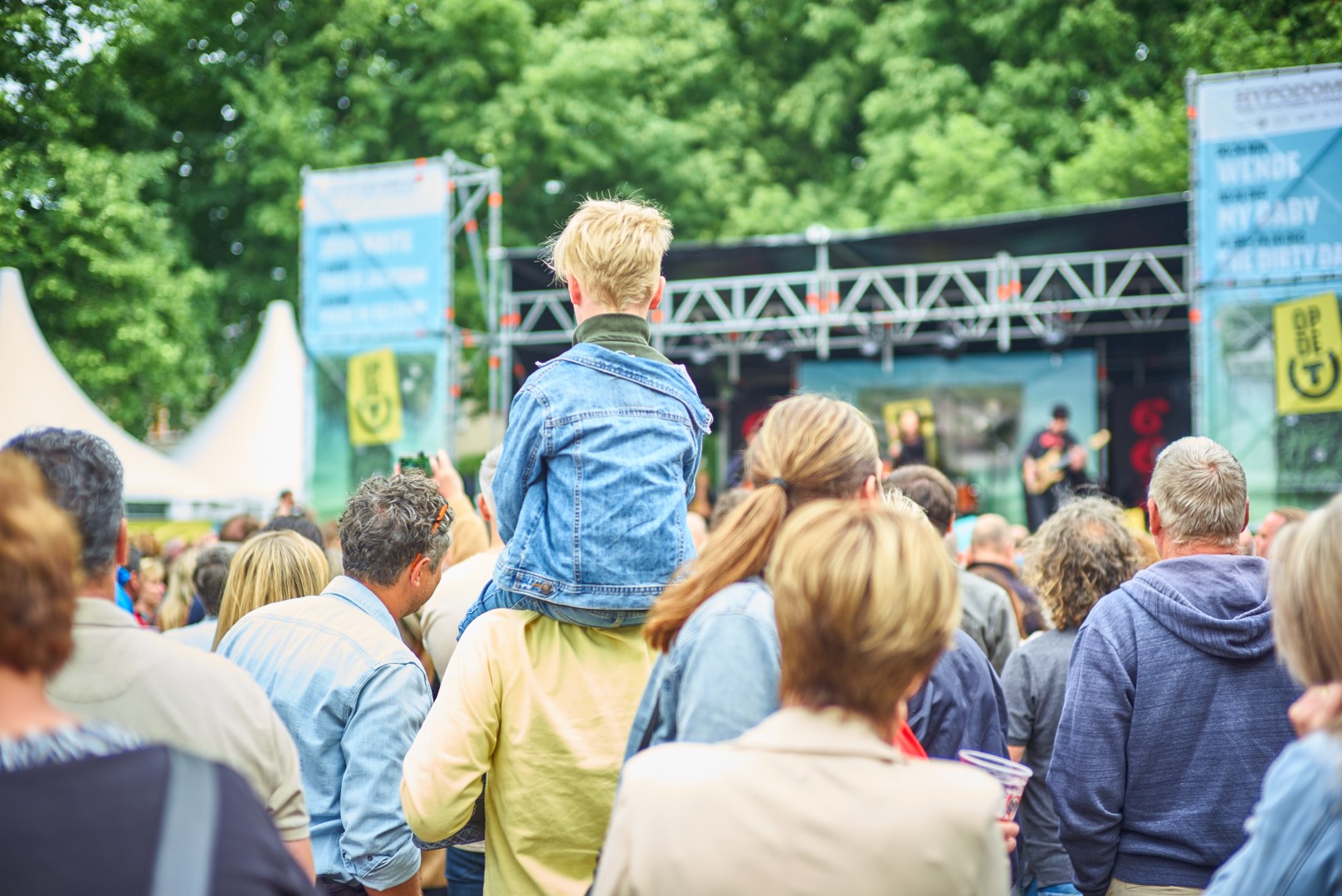 Jong kind zit op schouders tijdens concert.