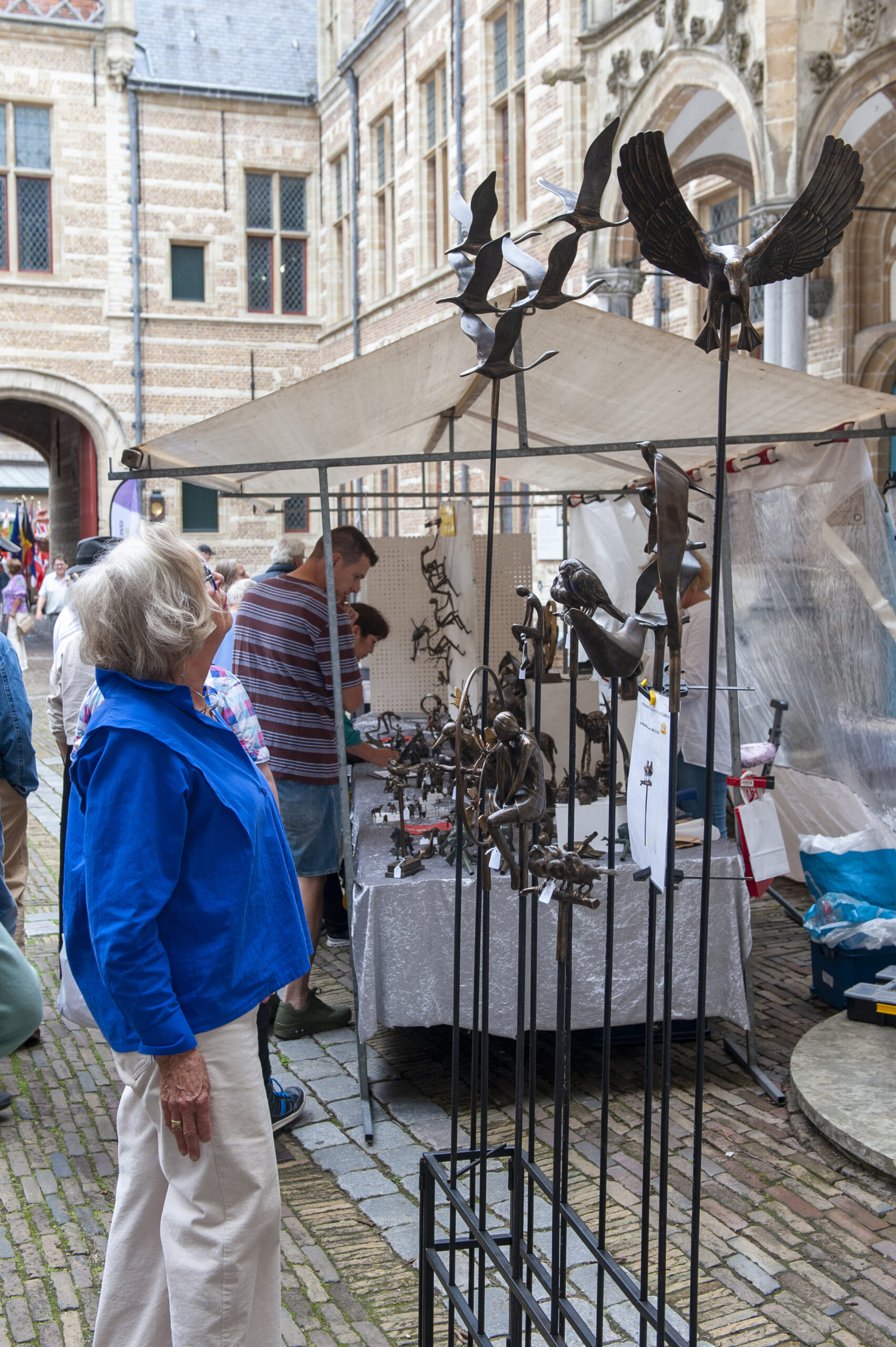 Vrouw bewondert metalen kunst op buitenmarkt.