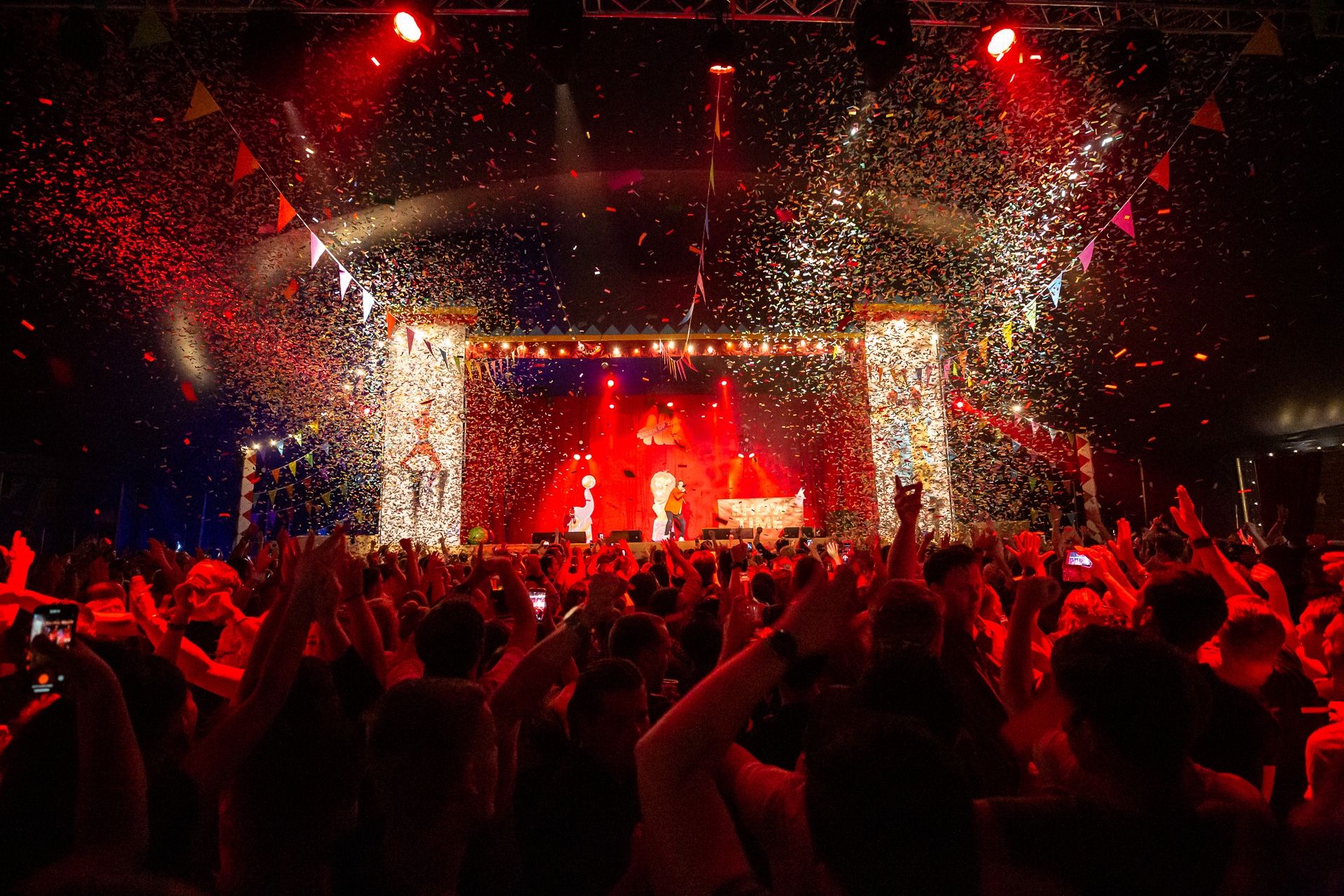 Concertpubliek met kleurrijke confetti en rode verlichting