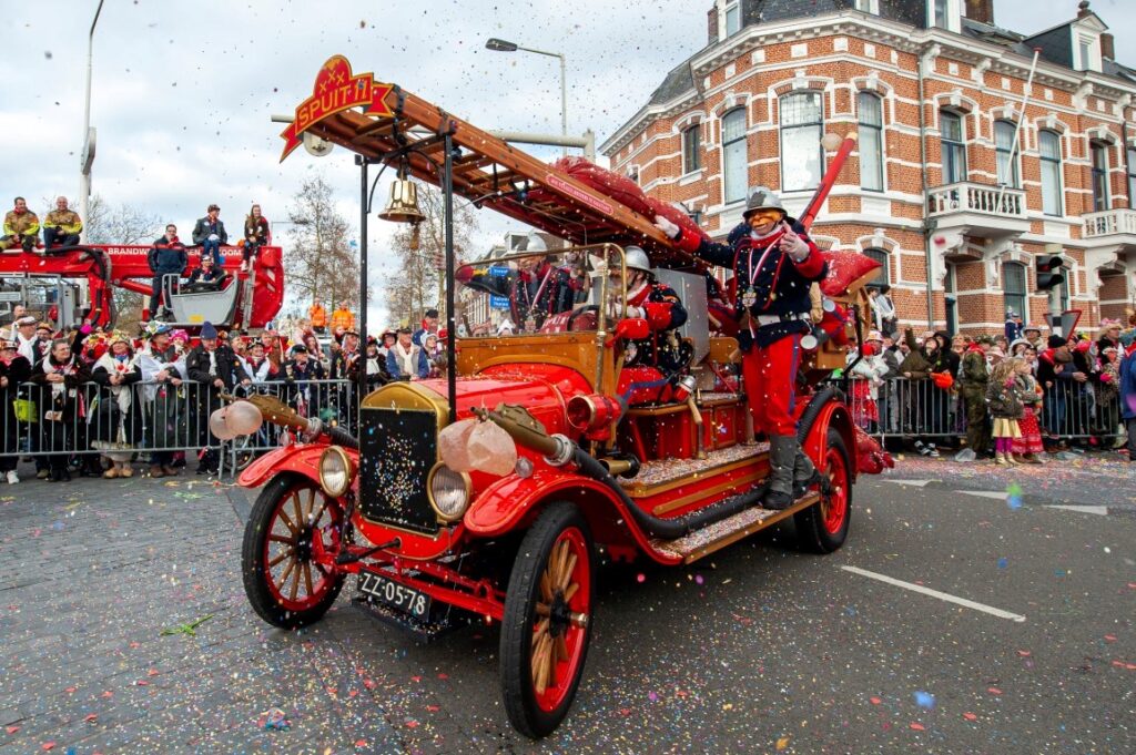 Carnavalsoptocht met antieke brandweerwagen en toeschouwers